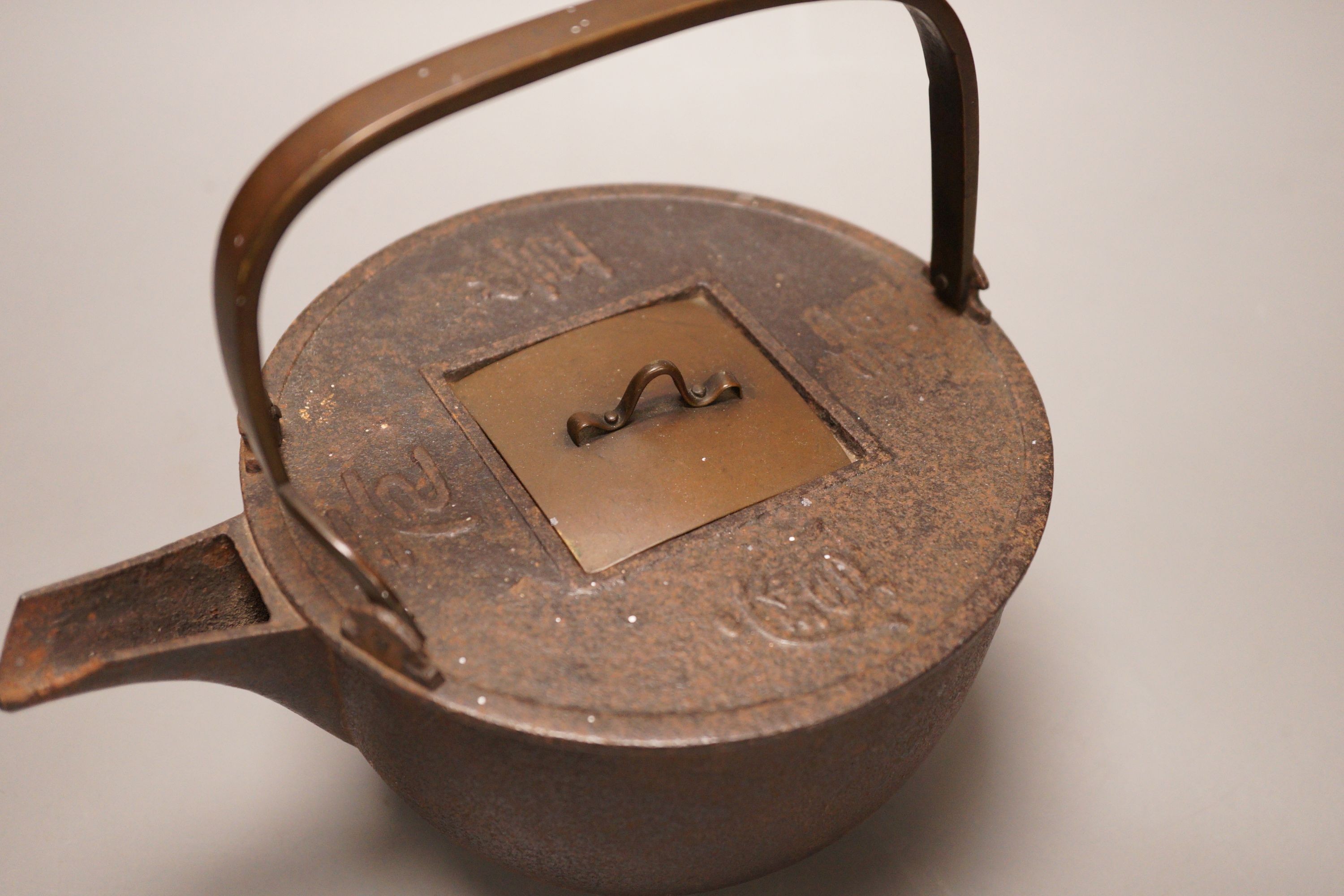 A Japanese cast iron and bronze teapot on tripod stand, inscribed, 19cm wide including spout